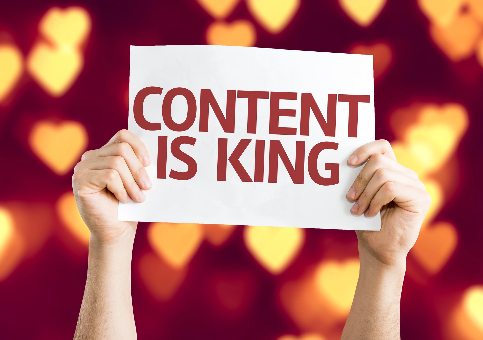 Hands holding a sign with 'CONTENT IS KING' text against a blurred warm-toned background